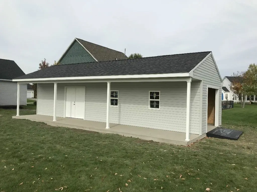 A white building with black roof and a porch.