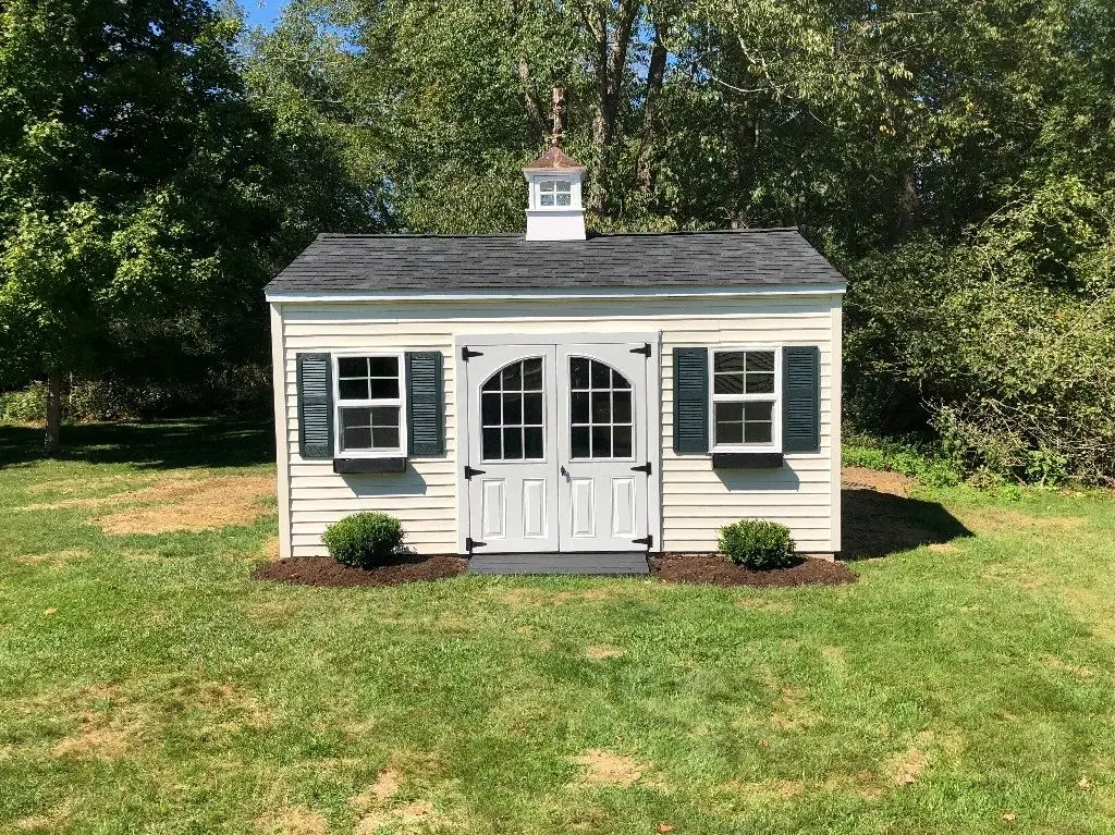 A small white shed with two windows and shutters.