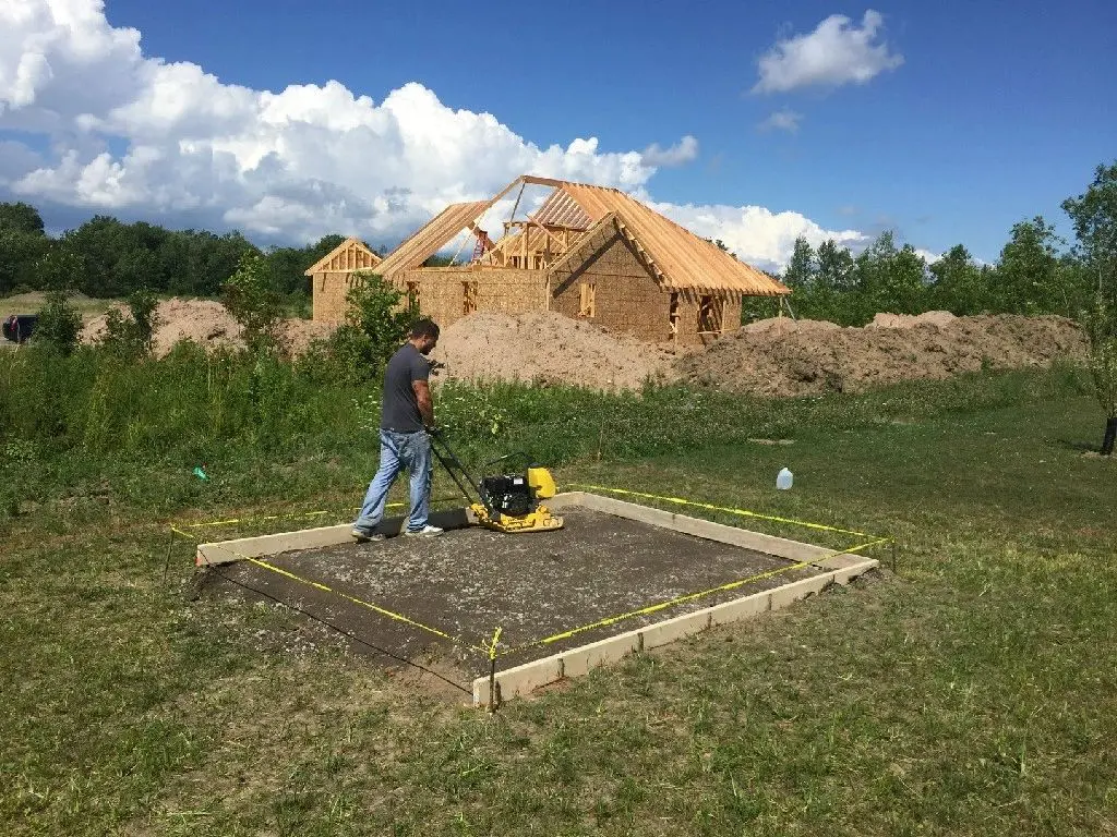 A man standing on top of dirt ground next to a pile of wood.