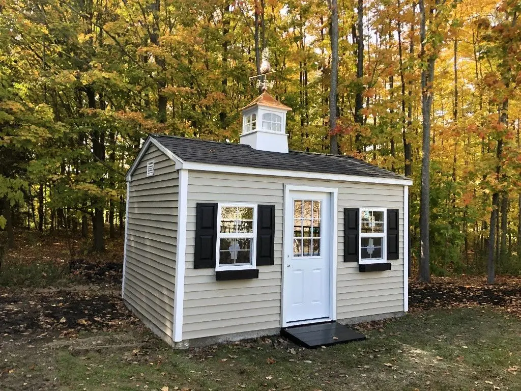 a shed with a white door, two windows, and a cupola