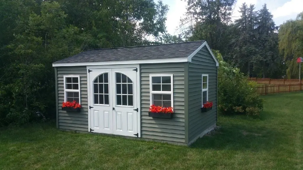 A green shed with two windows and red flowers.