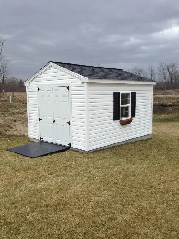 A white shed with black shutters and a ramp.