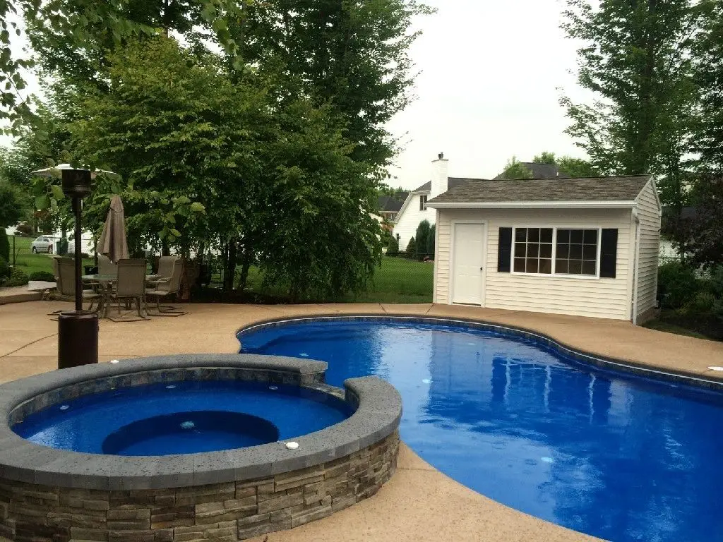 A pool with a hot tub and a gazebo in the background.