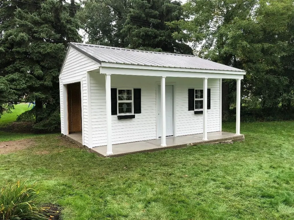A white shed with a porch and windows.