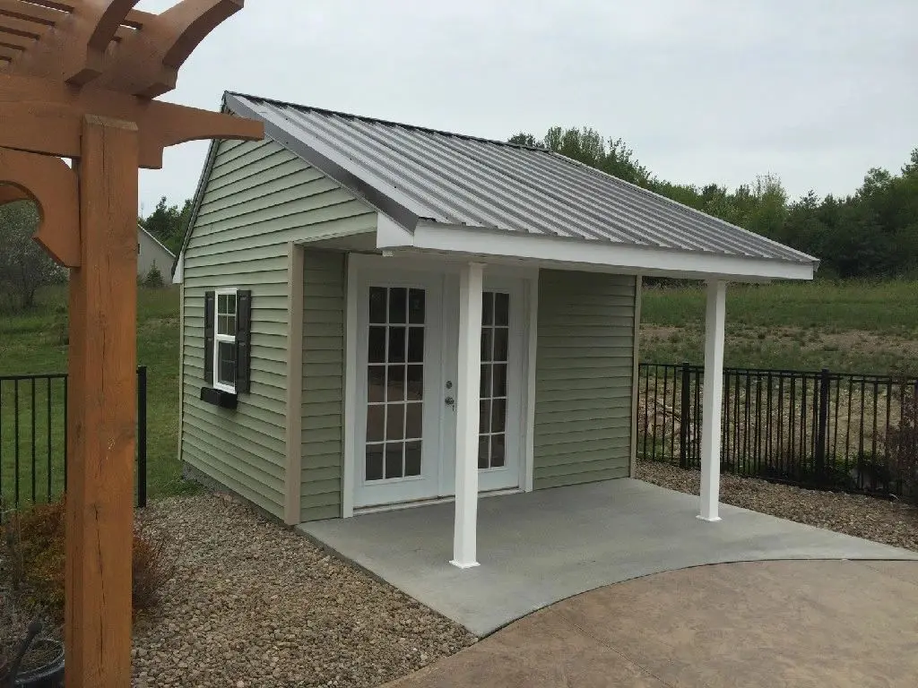 A small green shed with a porch and a pergola.