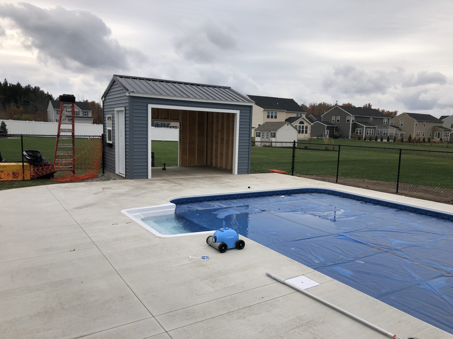 A pool with a shed and a ladder in the background.