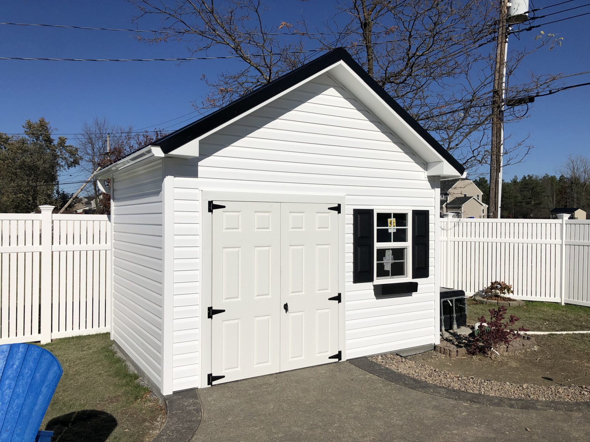 A white shed with two black shutters and a black door.