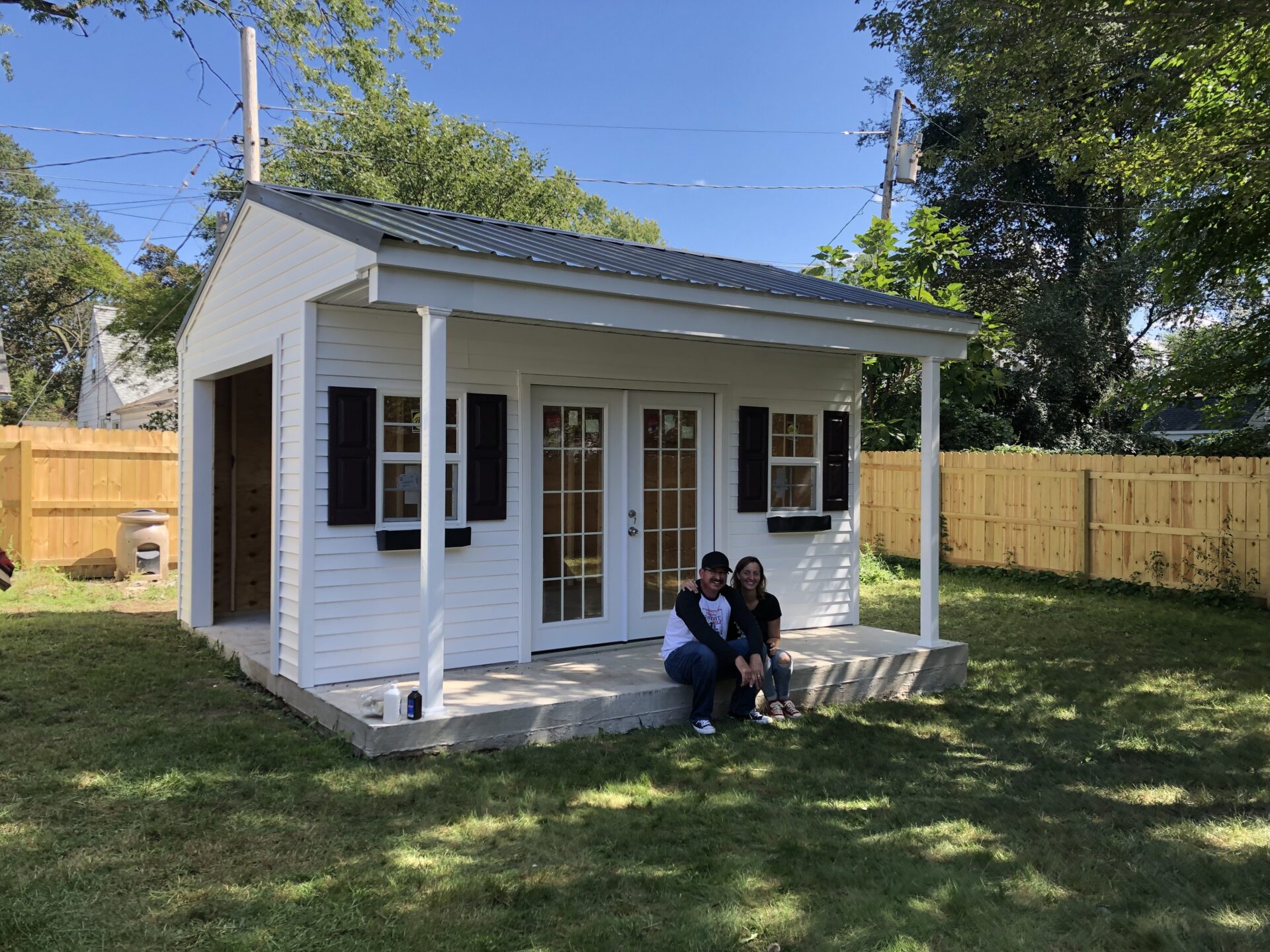 Two people sitting on a bench in front of a white shed.