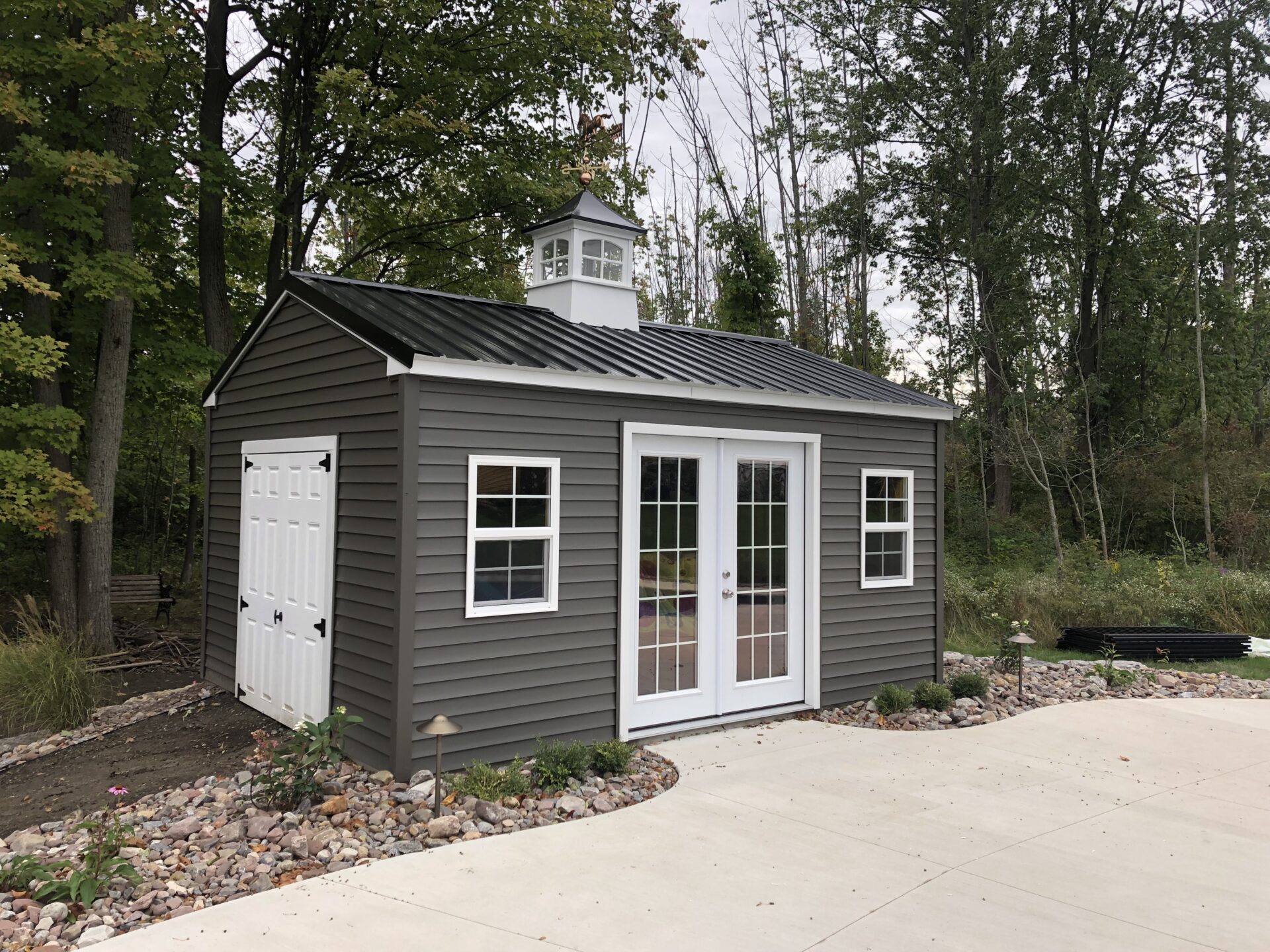 A shed with two doors and windows in the middle of a driveway.