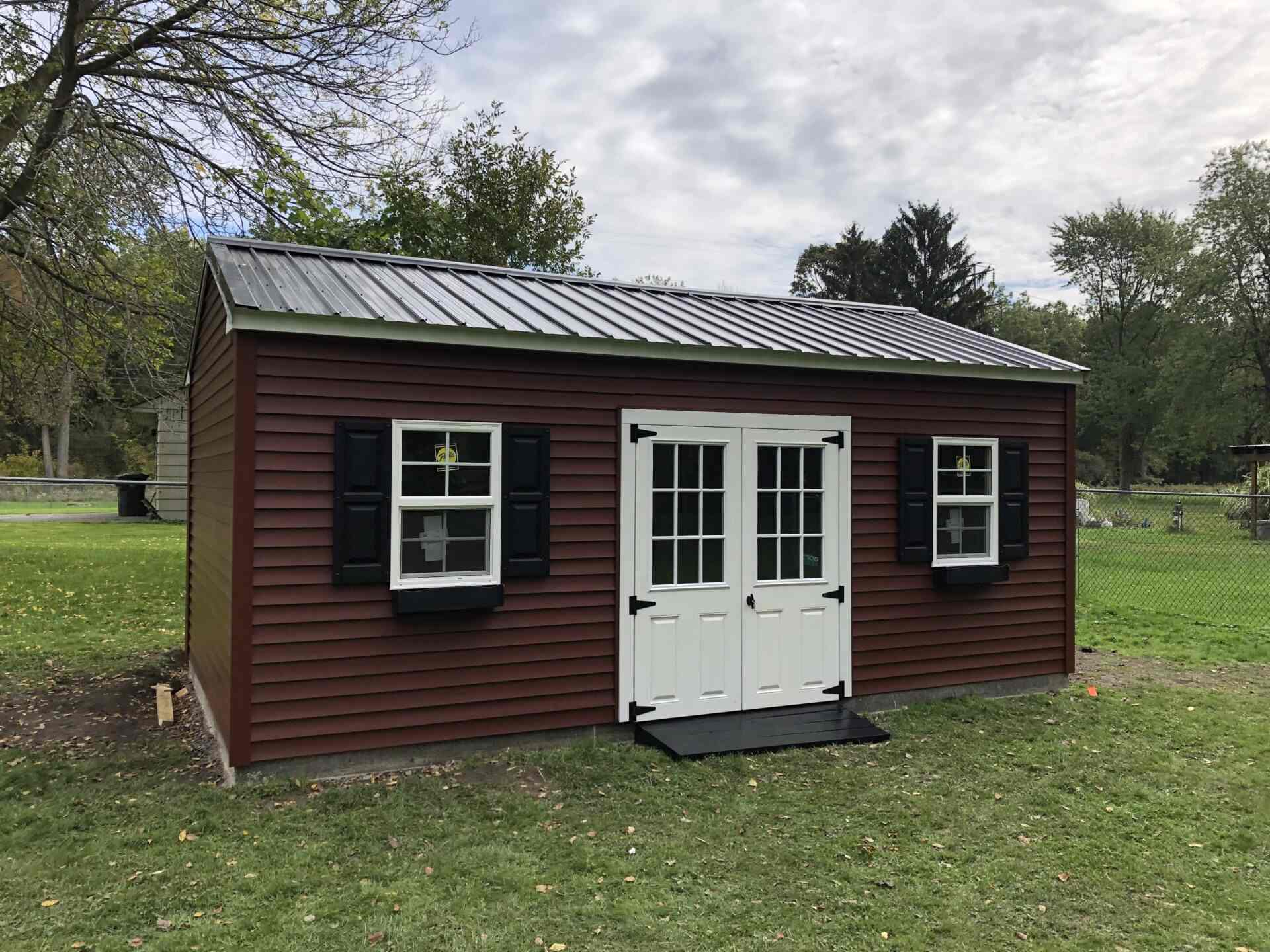 A brown shed with two windows and black shutters.