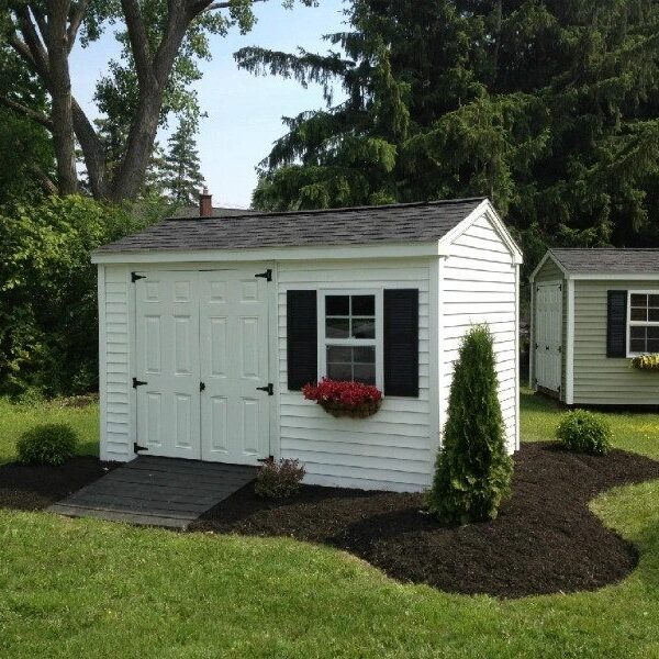 A white shed with black shutters and flowers on the window.